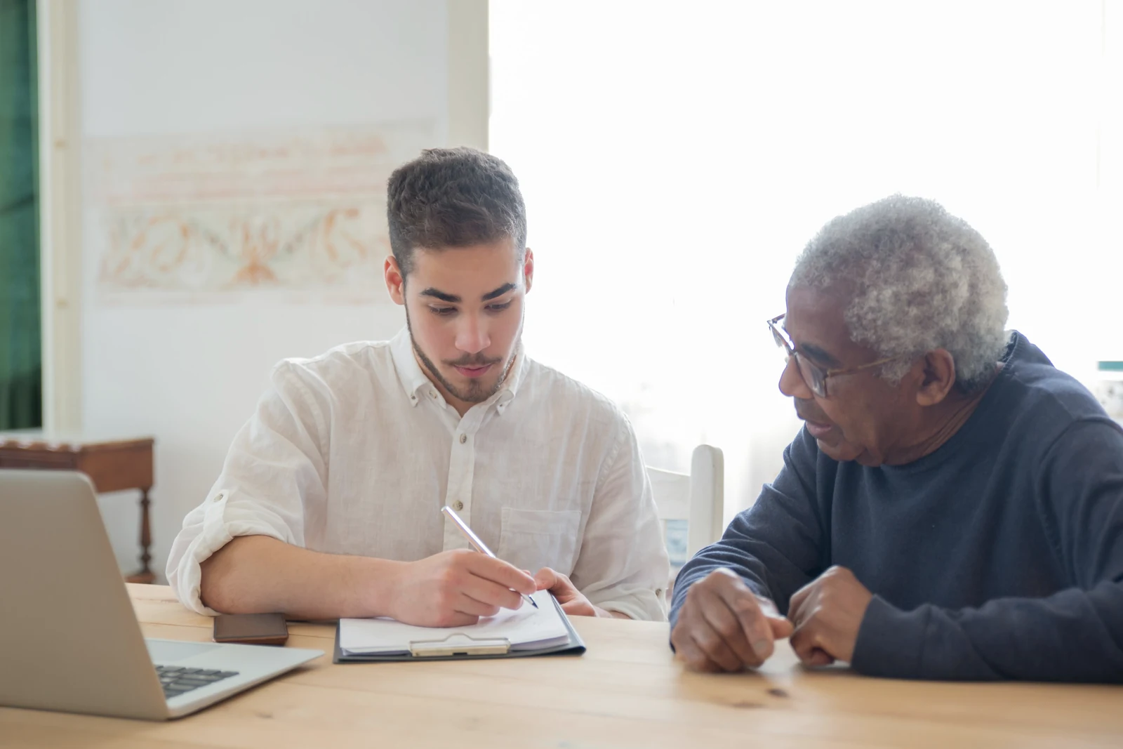A senior man and a younger adult family member reviewing a laptop and paperwork together at home while planning Super Visa insurance costs